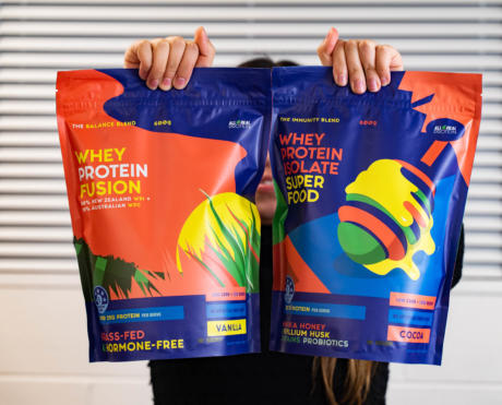 Two hands holding colourful All Real Protein stand up pouch product